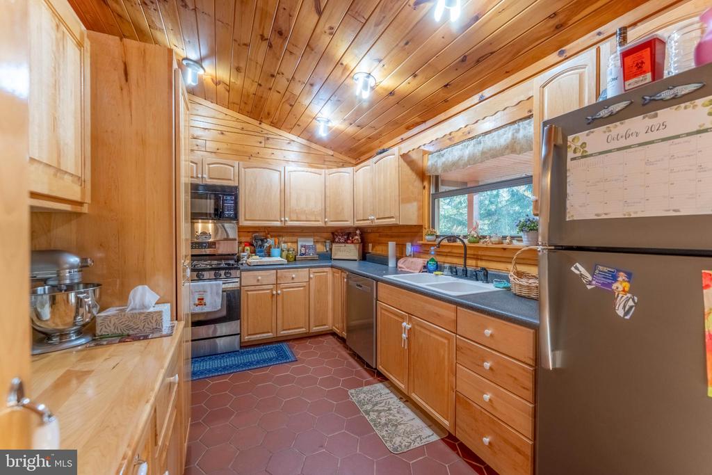 Kitchen with honey-colored wood cabinetry, a wood-plank ceiling, and reddish hexagonal floor tile.