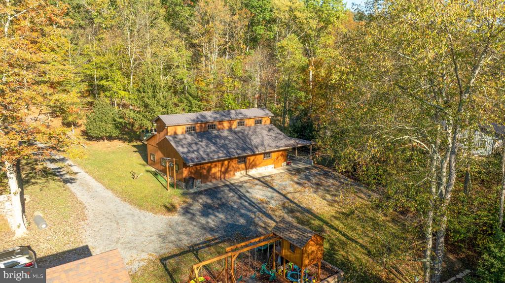 Aerial view of a wood-sided home surrounded by autumn trees, with a gravel driveway and playset.