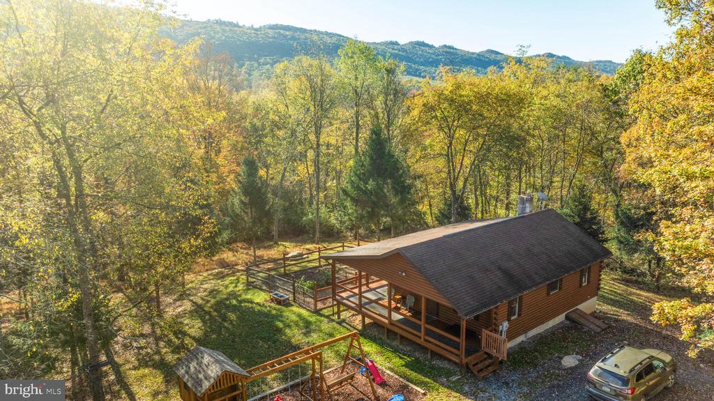 Cabin with a large deck in an autumn woodland, with mountains beyond.
