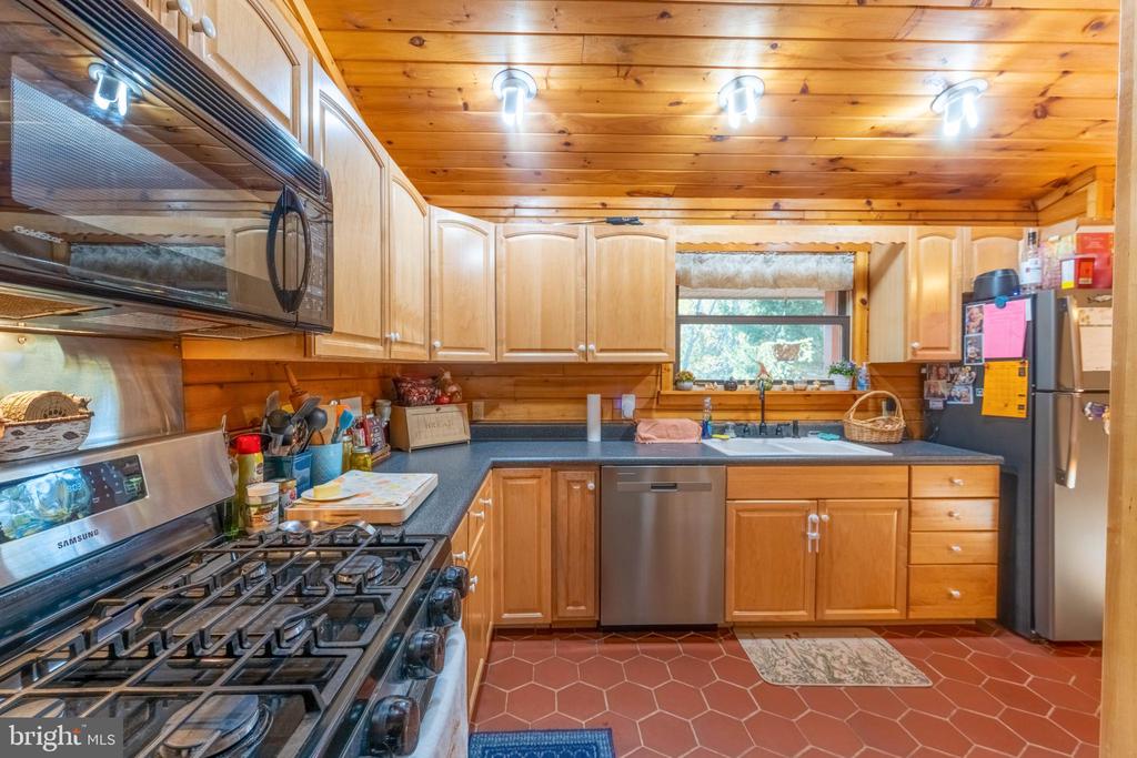 Kitchen with honey-colored wood cabinetry and ceiling, a stainless gas range, and terracotta tile floor.
