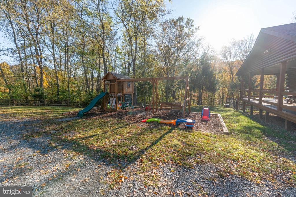 Backyard playset with a slide and swings beside a covered wooden deck, surrounded by autumn trees.