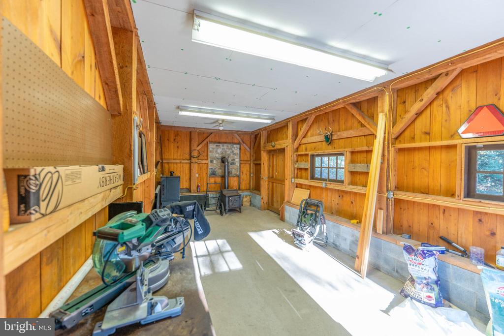Wooden workshop with exposed rafters, woodworking tools, and sunlight streaming across the concrete floor.