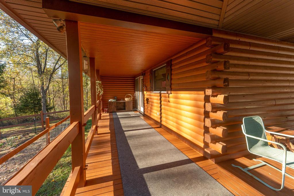 Covered log-cabin porch with a long gray rug and wooded autumn view.