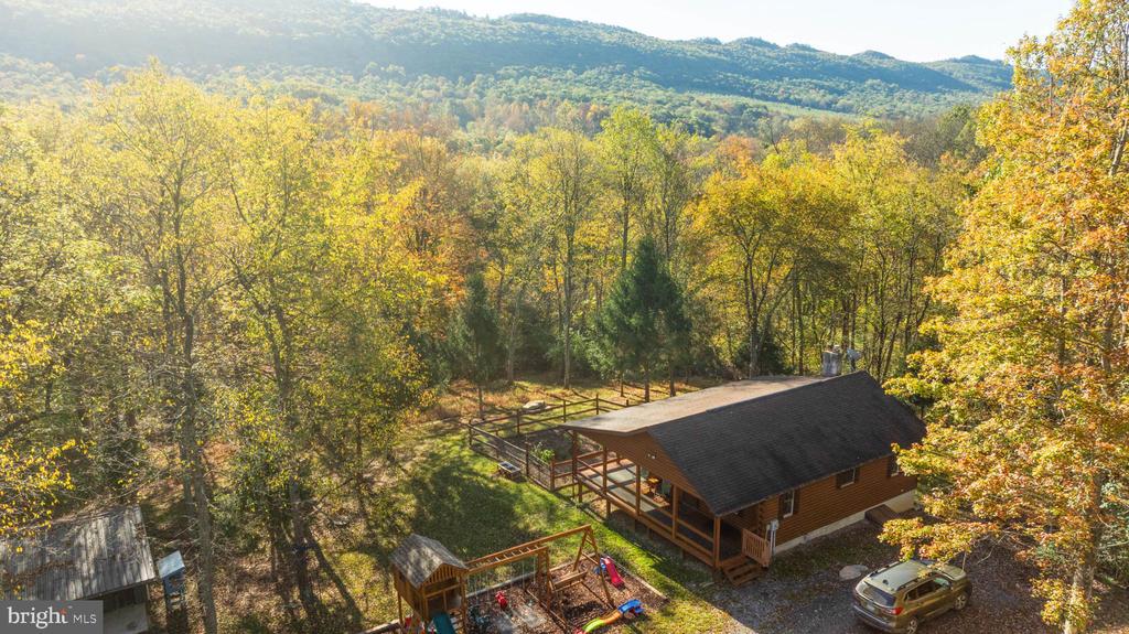 Aerial view of a cabin among autumn trees, with wooded mountain ridges beyond.