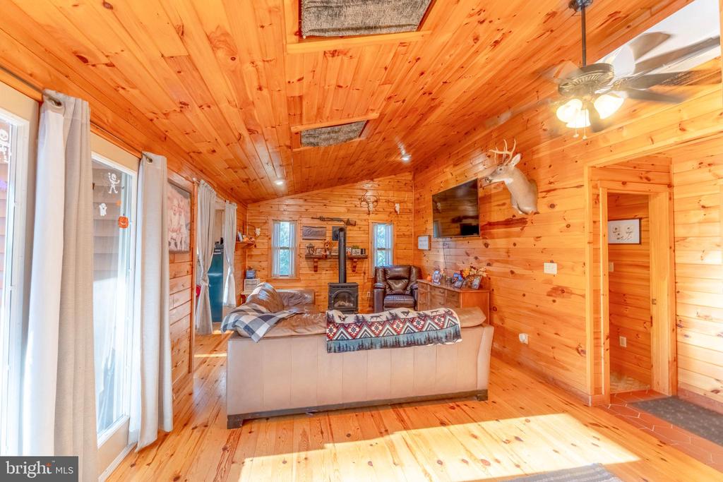 Wood-paneled living room with a sofa, wood stove, ceiling fan, and mounted deer head.