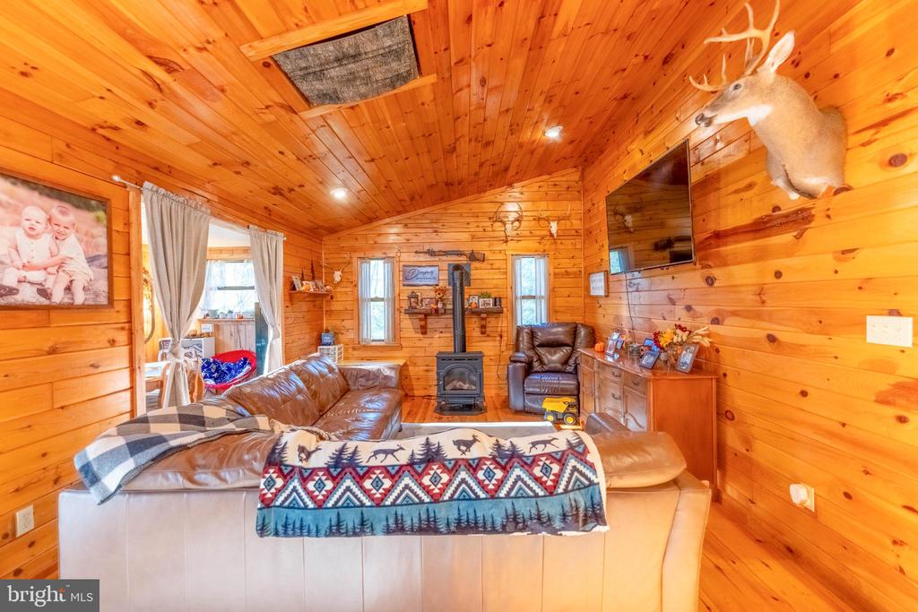 Cabin living room with a vaulted pine ceiling, leather seating, and a freestanding wood stove.
