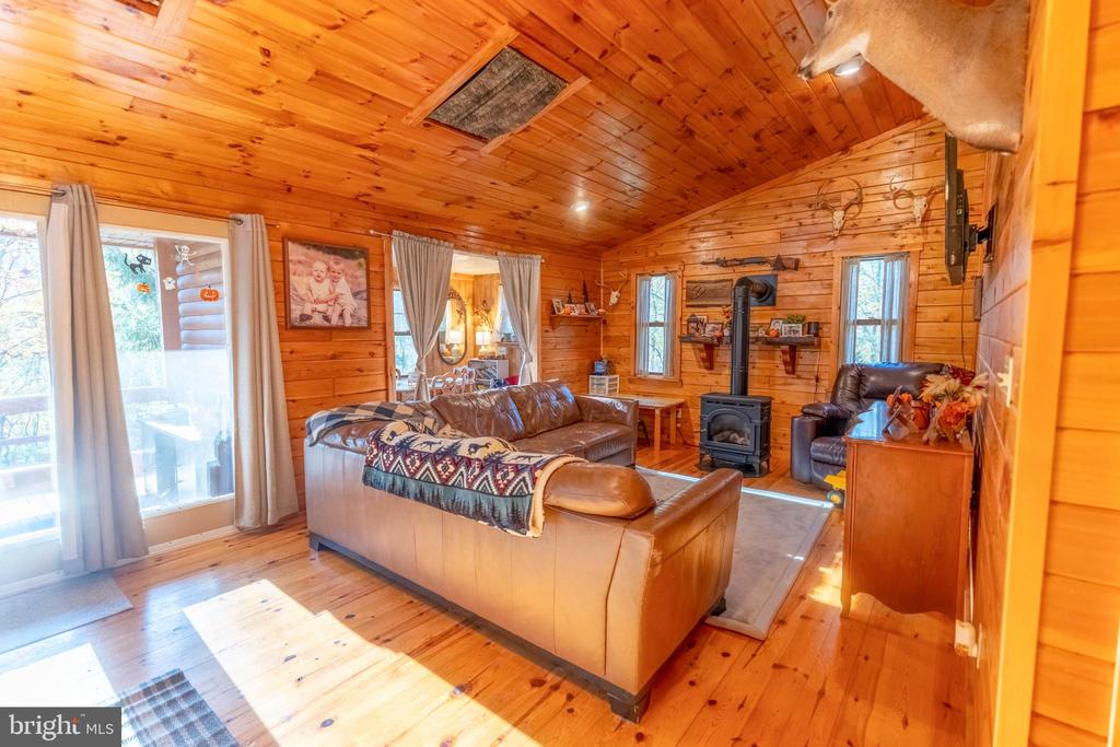 Wood-paneled living room with leather seating, a freestanding wood stove, and sunlight through glass doors.