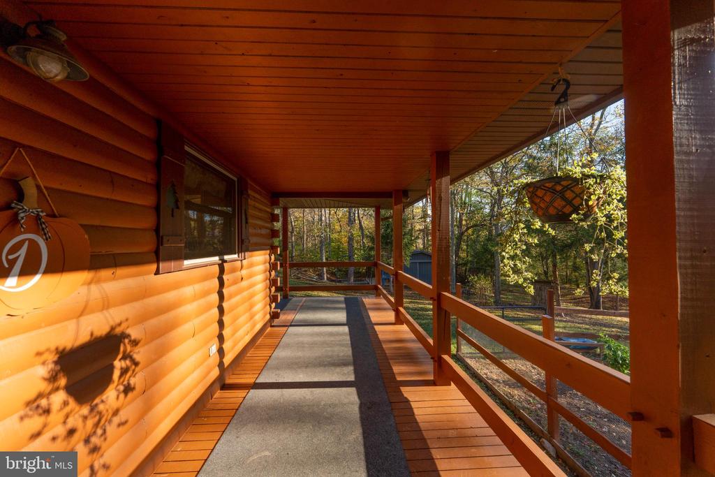 Covered log home porch with a wooden ceiling and railing overlooking autumn woods.