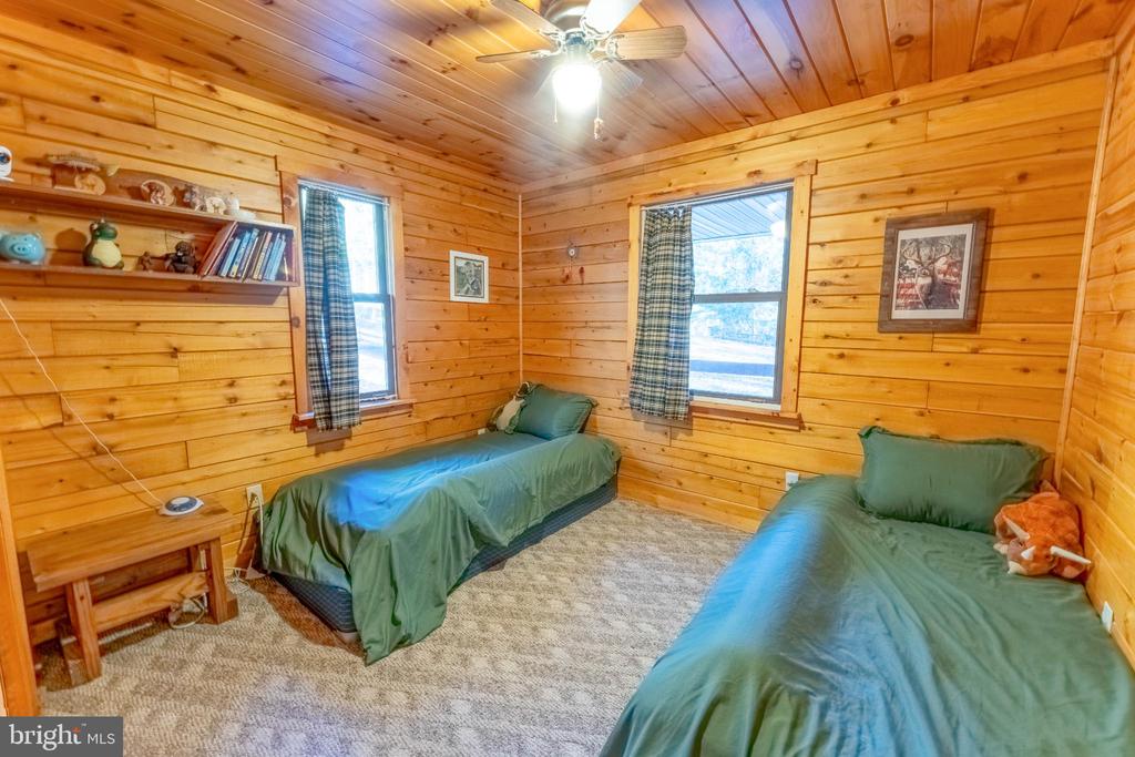 Wood-paneled bedroom with two twin beds, green bedding, and a vaulted ceiling.