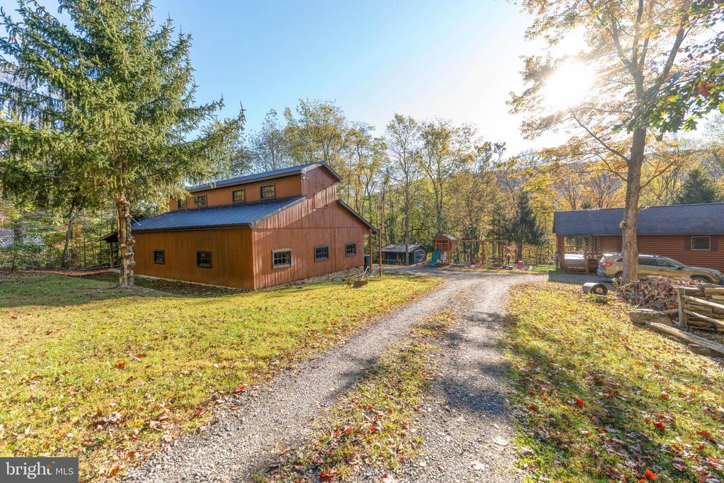 Wooded property with a brown barn-style building, gravel driveway, smaller cabin, and playground.