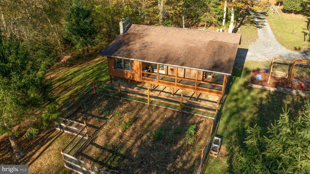 Aerial view of a brown-sided home with a covered porch, fenced yard, and wooded surroundings.