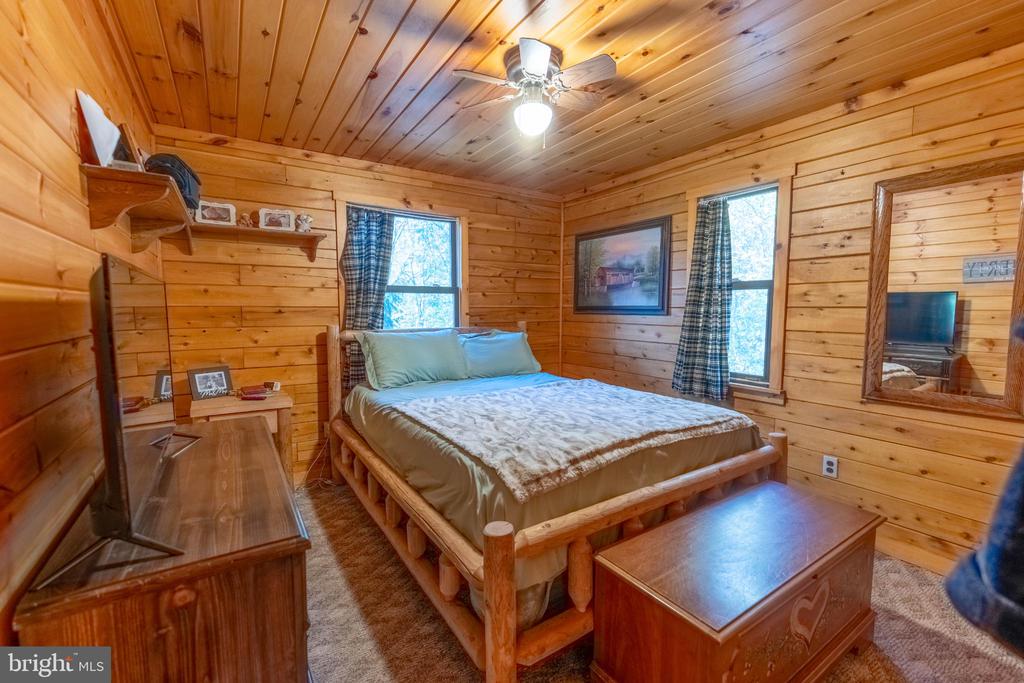 Wood-paneled bedroom with a log bed, two windows, and a ceiling fan.