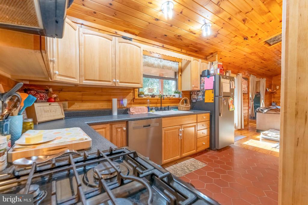 Kitchen with wood cabinetry and ceiling, a foreground gas range, and stainless-steel appliances.