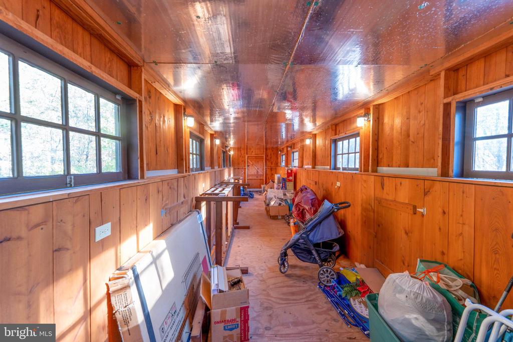 Long wood-paneled room with windows on both sides and stored items along the plywood floor.