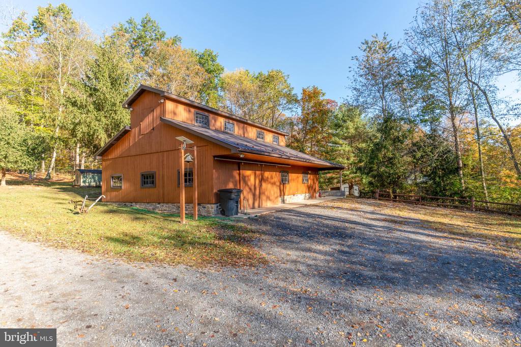 Brown timber-clad property with a stone foundation and broad gravel driveway among autumn trees.