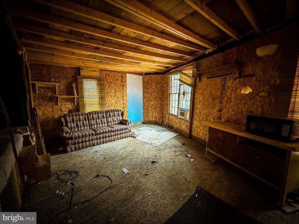Unfinished room with exposed plywood walls, a plaid sofa, and a window air conditioner.