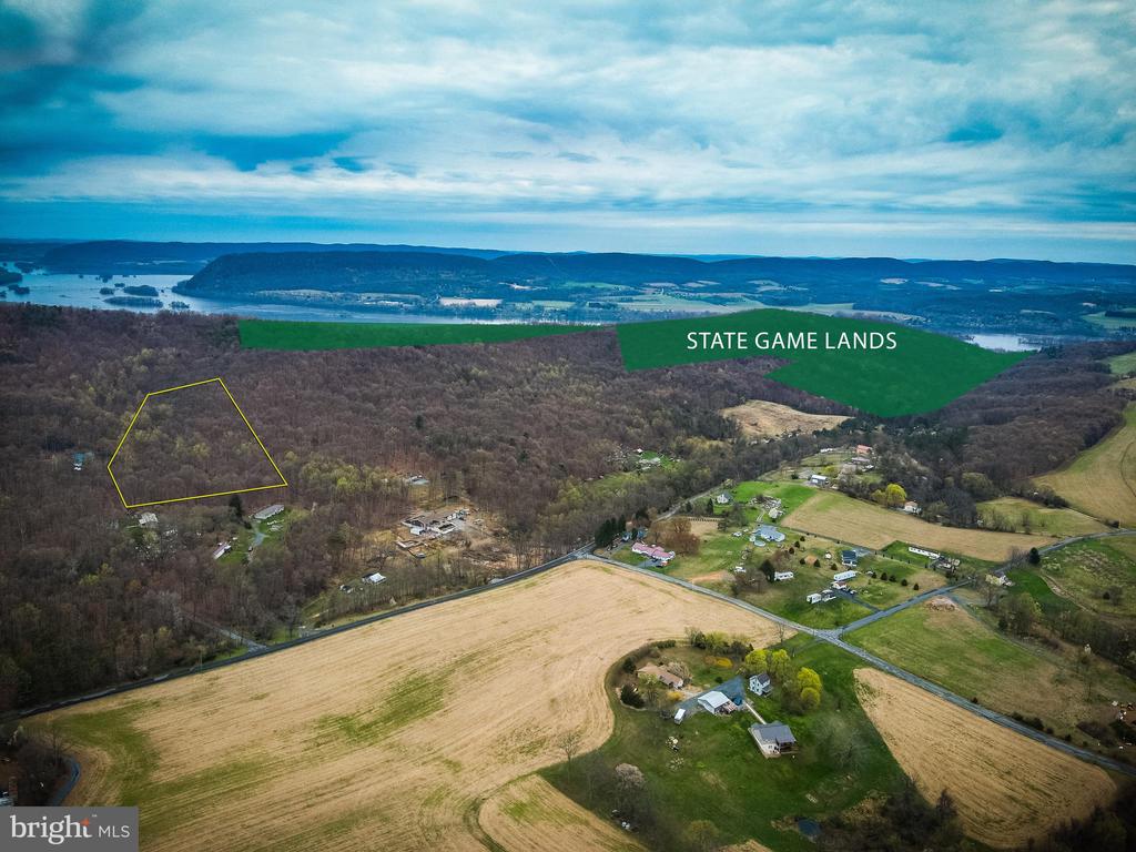 Aerial view of wooded property outlined in yellow, with fields, distant water, and State Game Lands nearby.