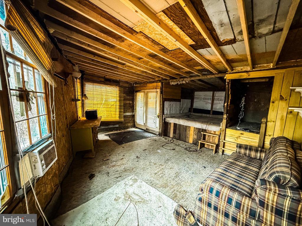 Rustic unfinished room with exposed ceiling joists, plaid couch, and built-in sleeping area.