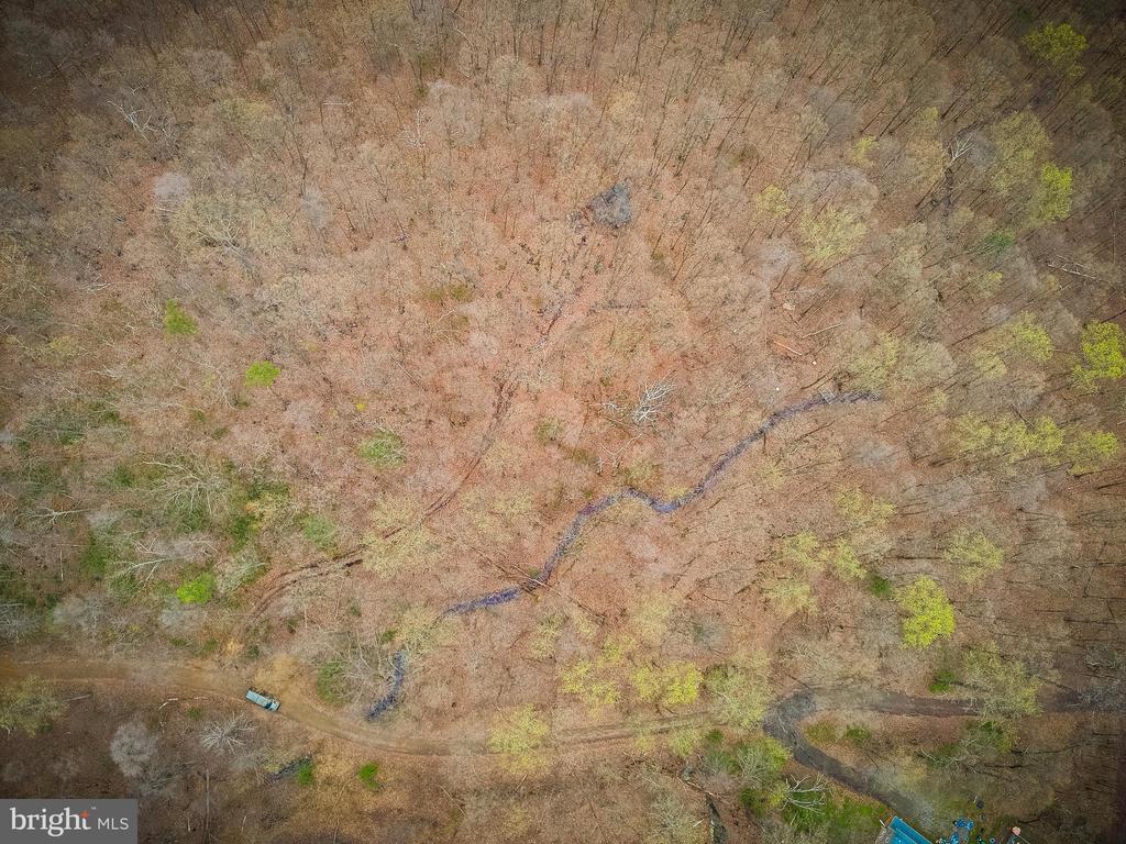 Aerial view of wooded land with a winding creek and dirt access road.