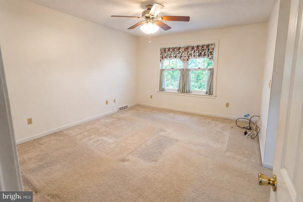 Empty carpeted bedroom with a ceiling fan and curtained window.