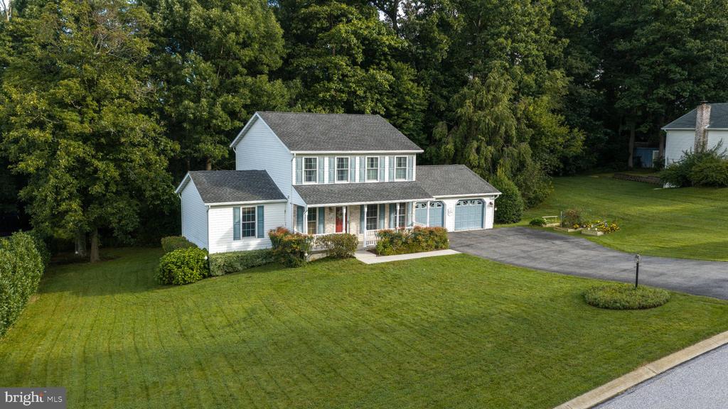 White two-story house with an attached garage, broad lawn, and wooded backdrop.