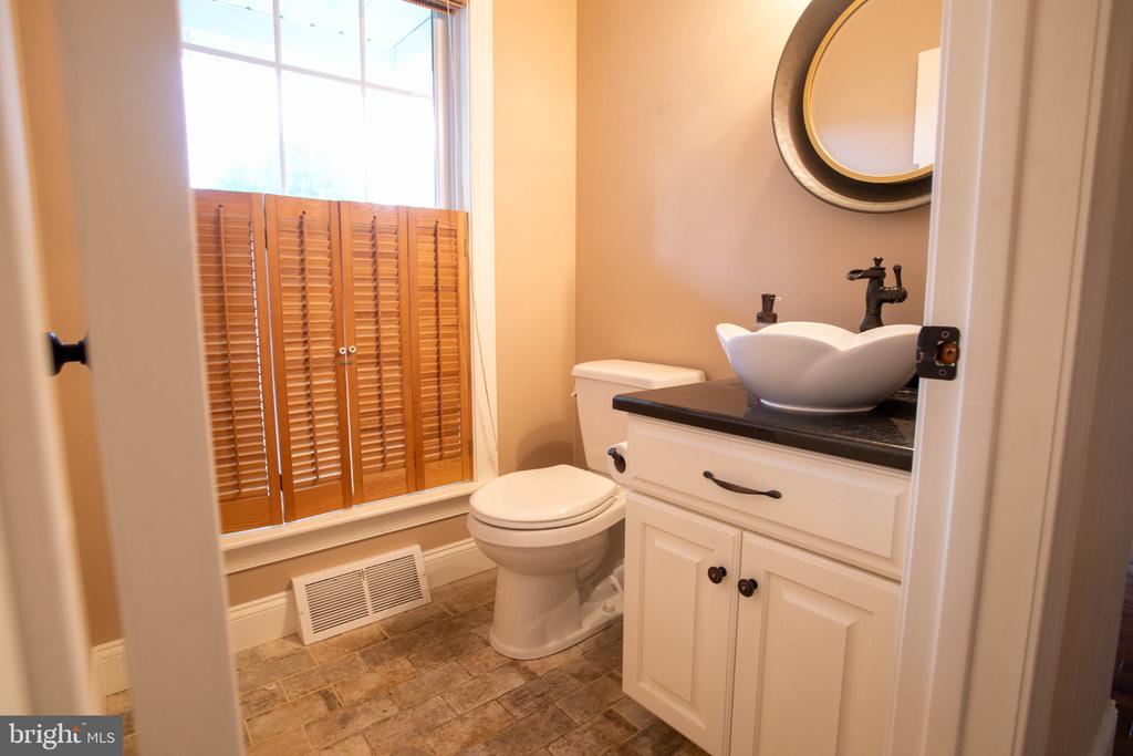 Bathroom with a vessel sink, white vanity, toilet, and shuttered window.