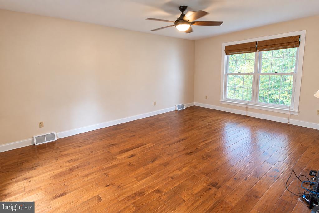 Empty room with hardwood floors, a ceiling fan, and a large window with wooden blinds.