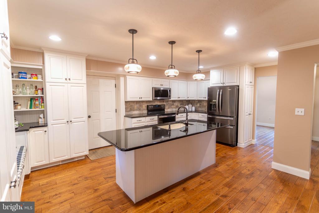 Kitchen with a large dark island, white cabinets, stainless steel appliances, and hardwood floors.