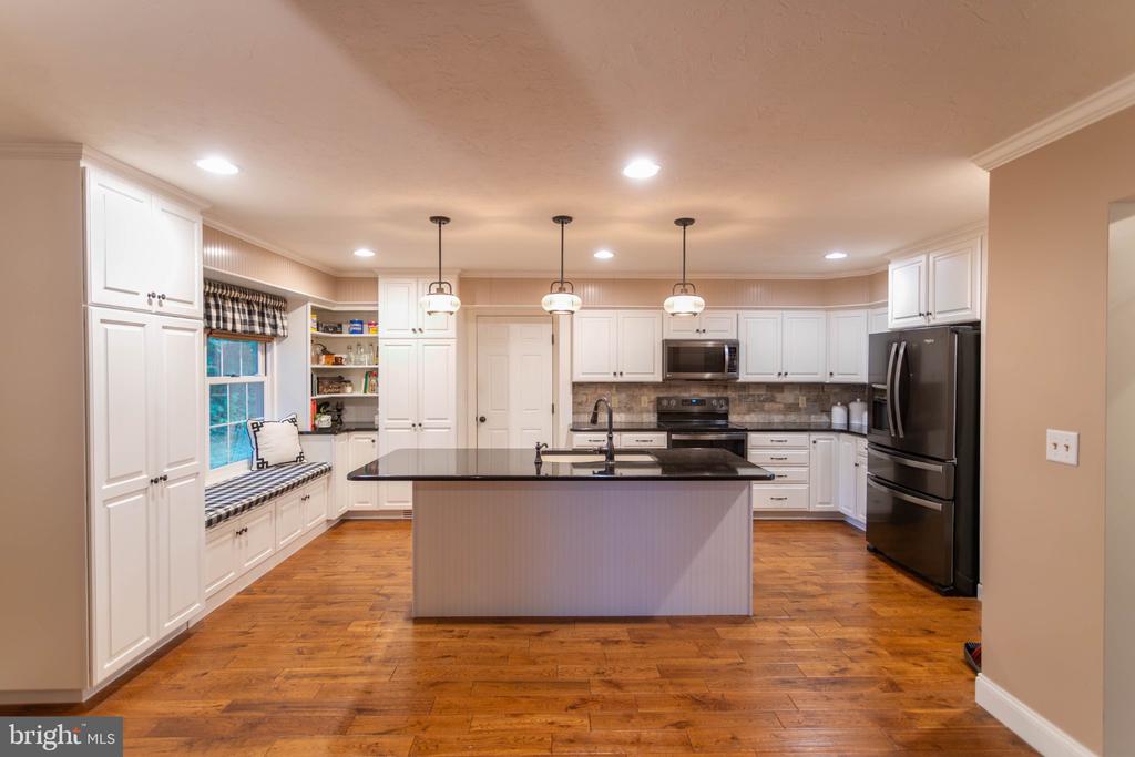 Kitchen with a large central island, white cabinetry, stainless appliances, and hardwood floors.