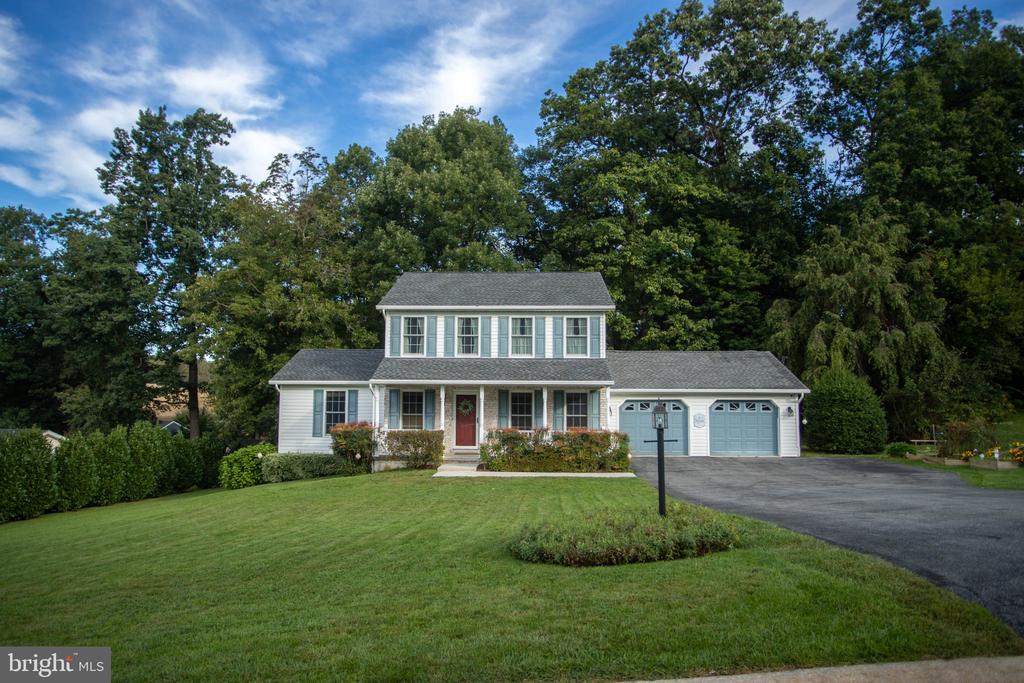 Two-story white home with a red front door, attached garage, and broad green lawn.