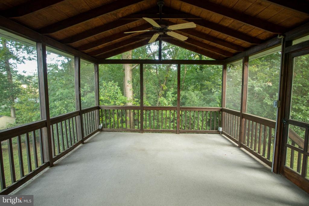 Screened porch with a wood-beamed ceiling, ceiling fan, and leafy wooded views.