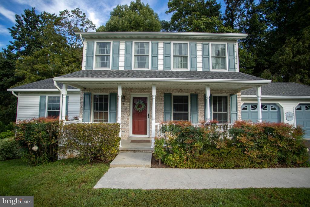 Two-story house with pale blue shutters, a covered porch, red front door, and attached garage.
