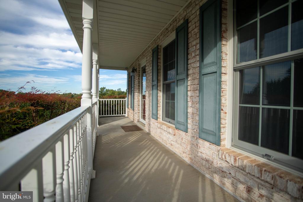 Covered porch with stone walls, teal shutters, and white railings overlooking trees.