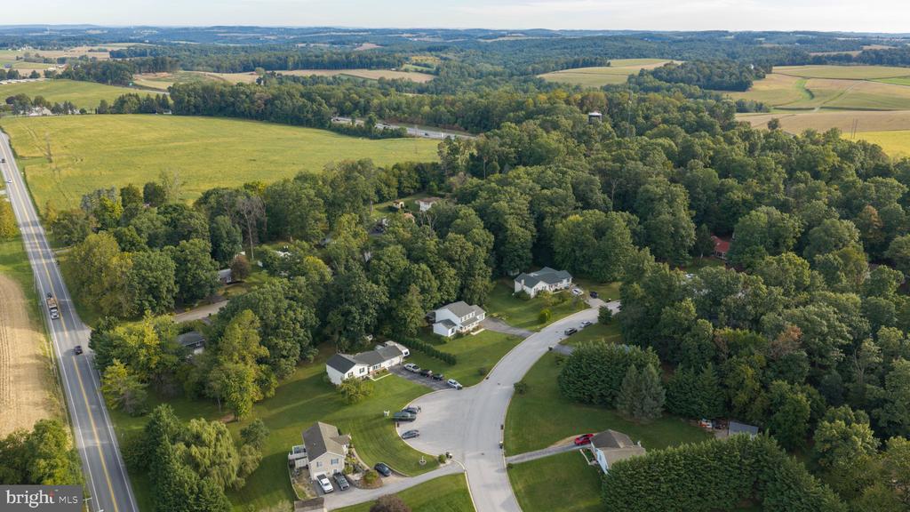 Aerial view of homes along a wooded cul-de-sac, with fields and farmland beyond.