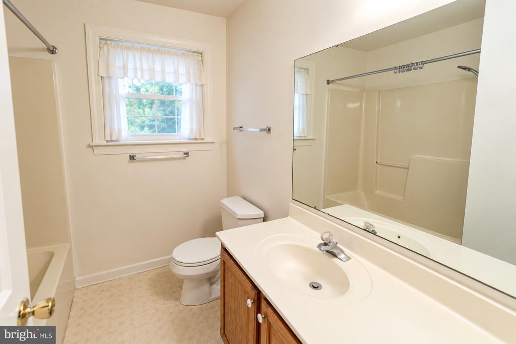 Bathroom with a wood vanity, large mirror, white tub and shower, and curtained window.