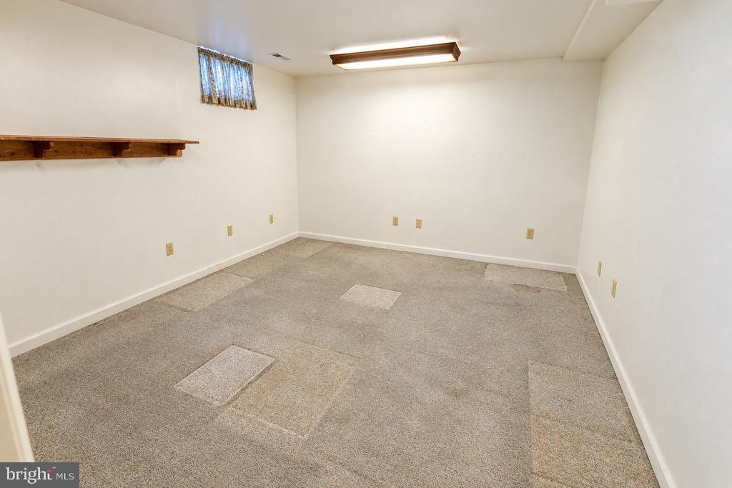 Empty carpeted room with a high window, wooden wall shelf, and visible carpet patches.