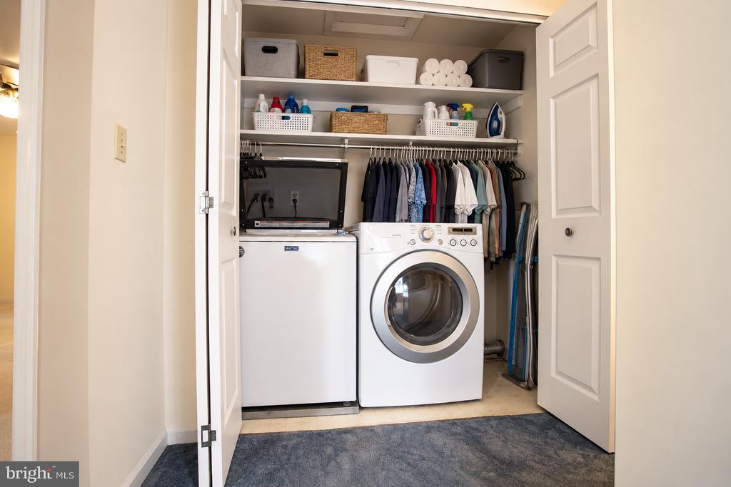 Laundry closet with washer and dryer, organized shelves, and hanging clothes.