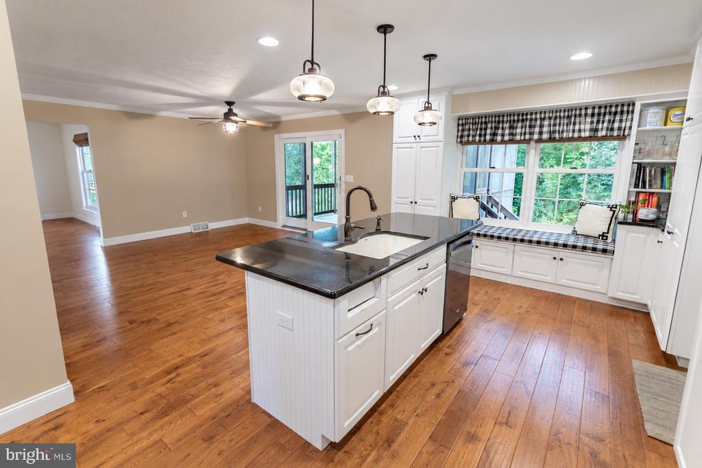 Open kitchen with a large island, hardwood floors, and a built-in window seat overlooking greenery.