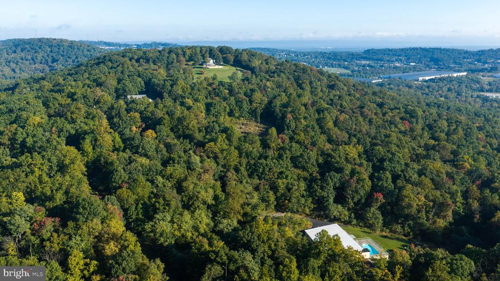 Aerial view of wooded rolling hills, with a home and pool among the trees and a river in the distance.