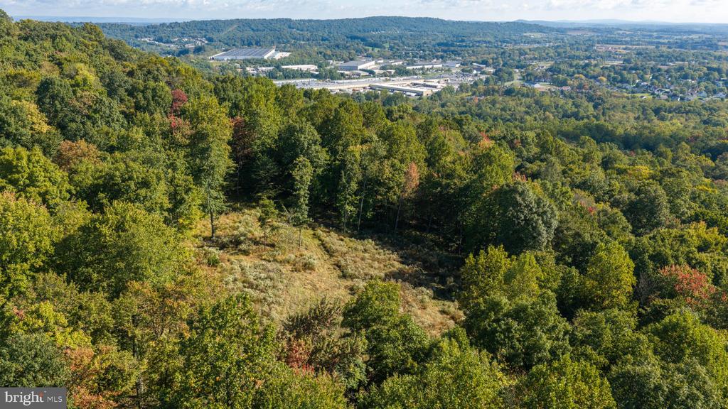 Aerial view of wooded land with a grassy clearing and distant buildings.