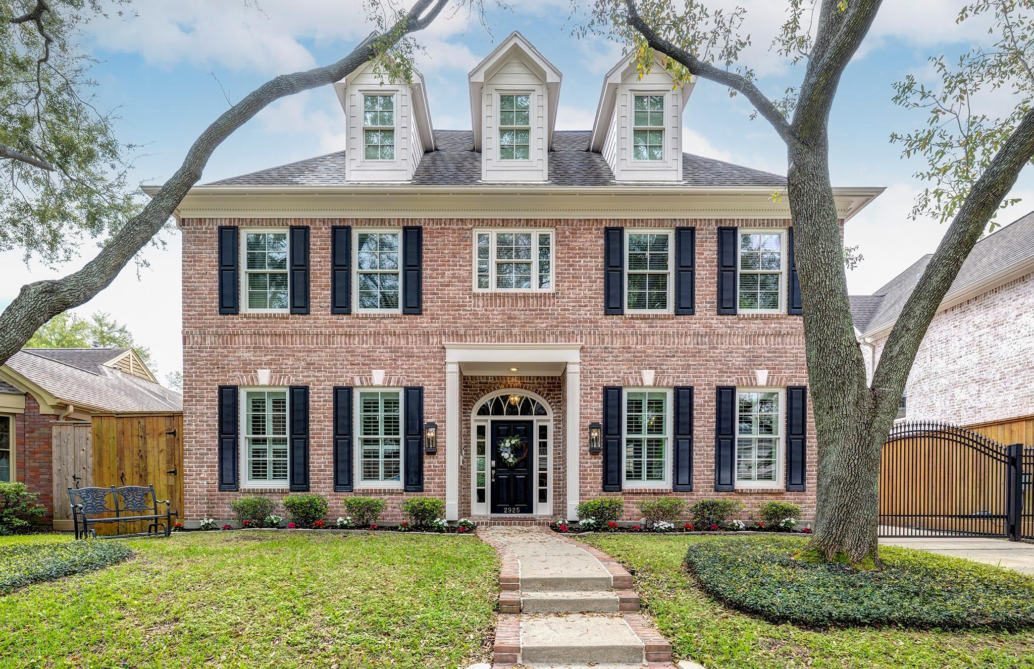 Two-story brick house with white dormers, dark shutters, and an arched front entrance.