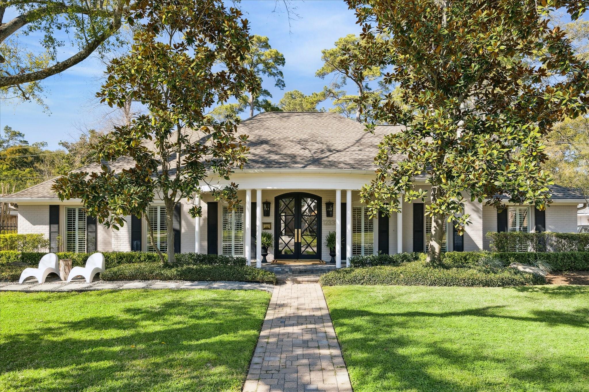 White brick home with a columned porch, black double doors, and a brick walkway through the lawn.