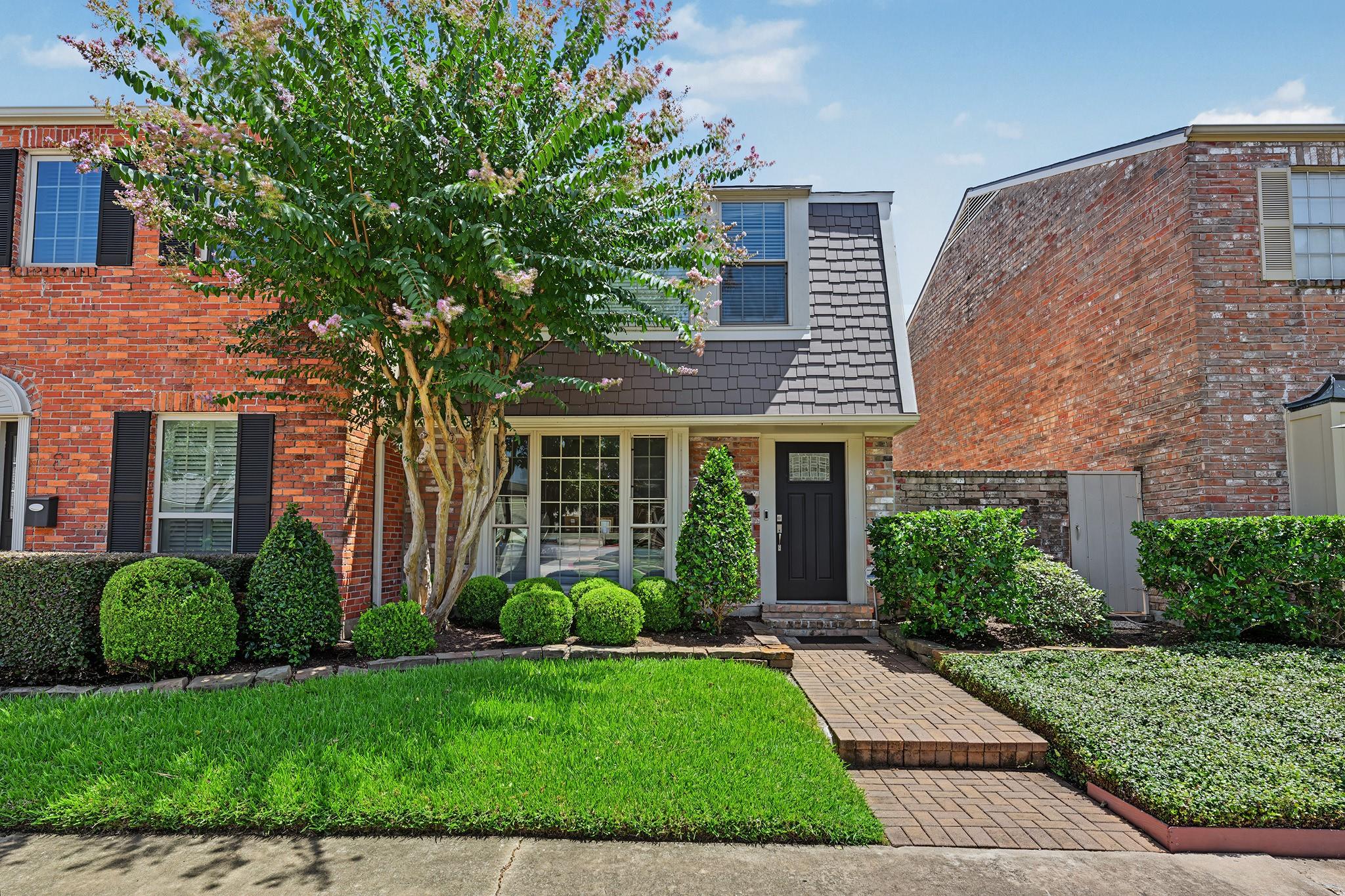 Brick townhouse with a flowering tree, trimmed shrubs, and a brick walkway to the front door.