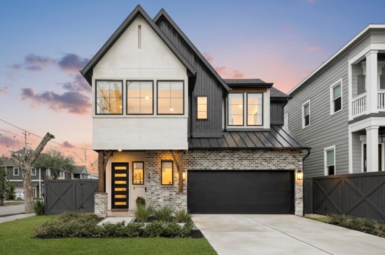 Modern two-story home with steep gables, brick facade, and a wide dark garage door at dusk.