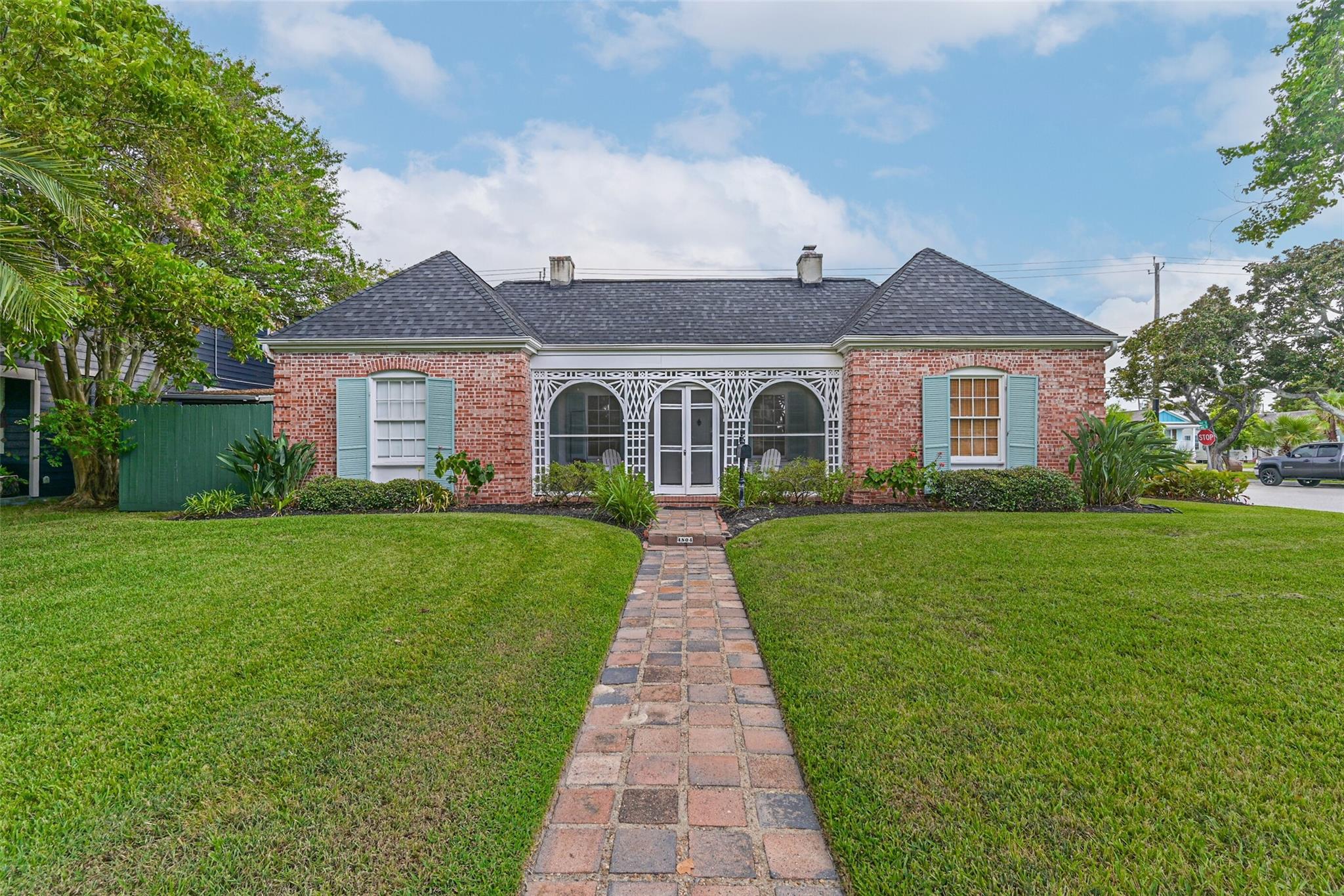 Red brick house with pale blue shutters, ornate white porch lattice, and a brick walkway across the lawn.