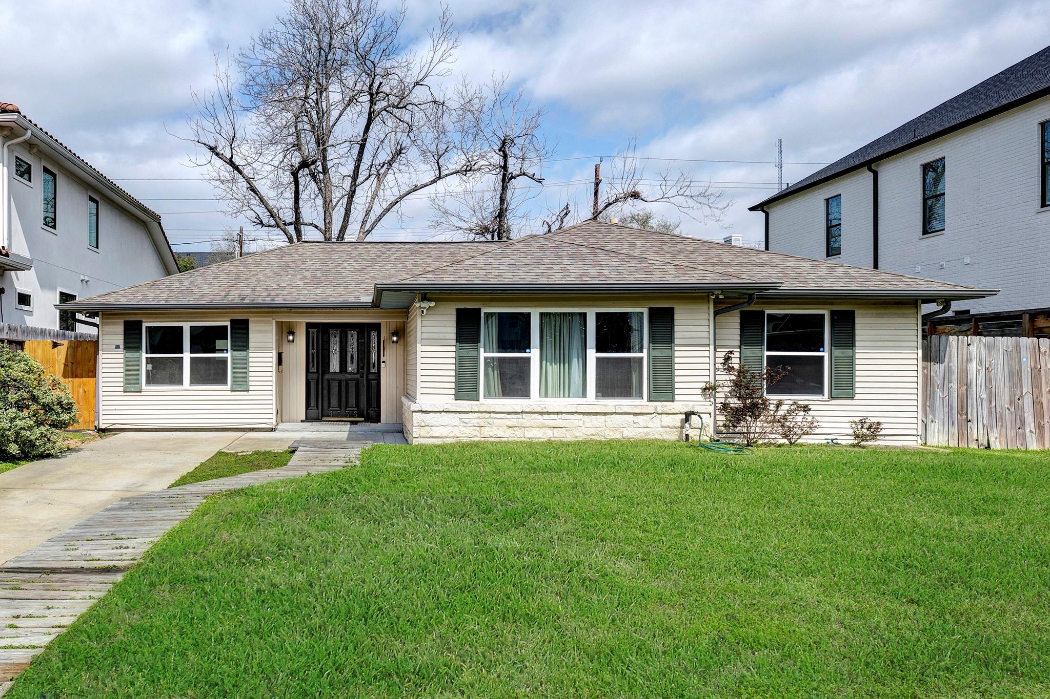 Single-story home with green shutters, stone facade accents, and a broad front lawn.