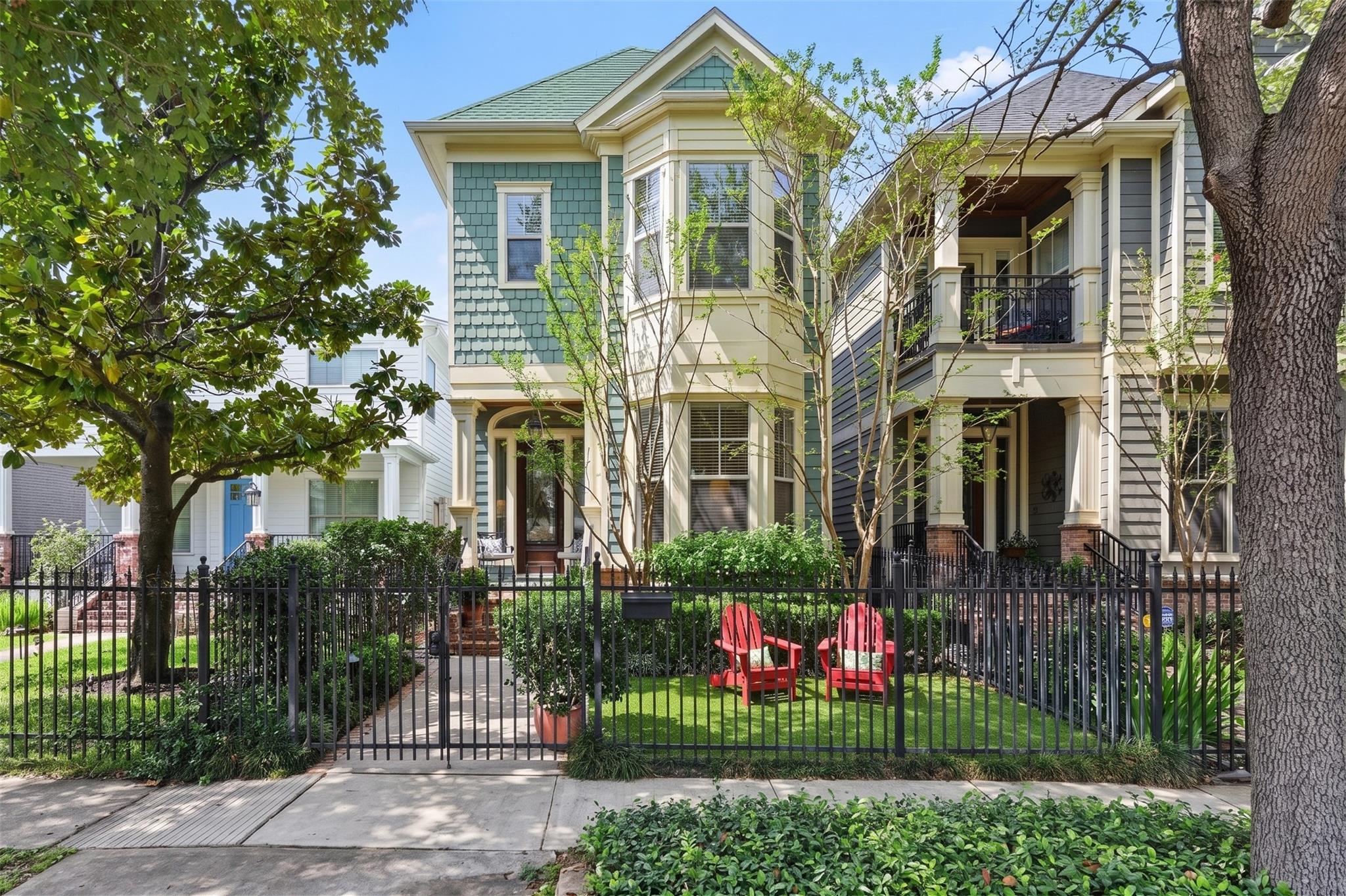 Attached homes with covered porches behind a black iron fence, with landscaped yards and red Adirondack chairs.