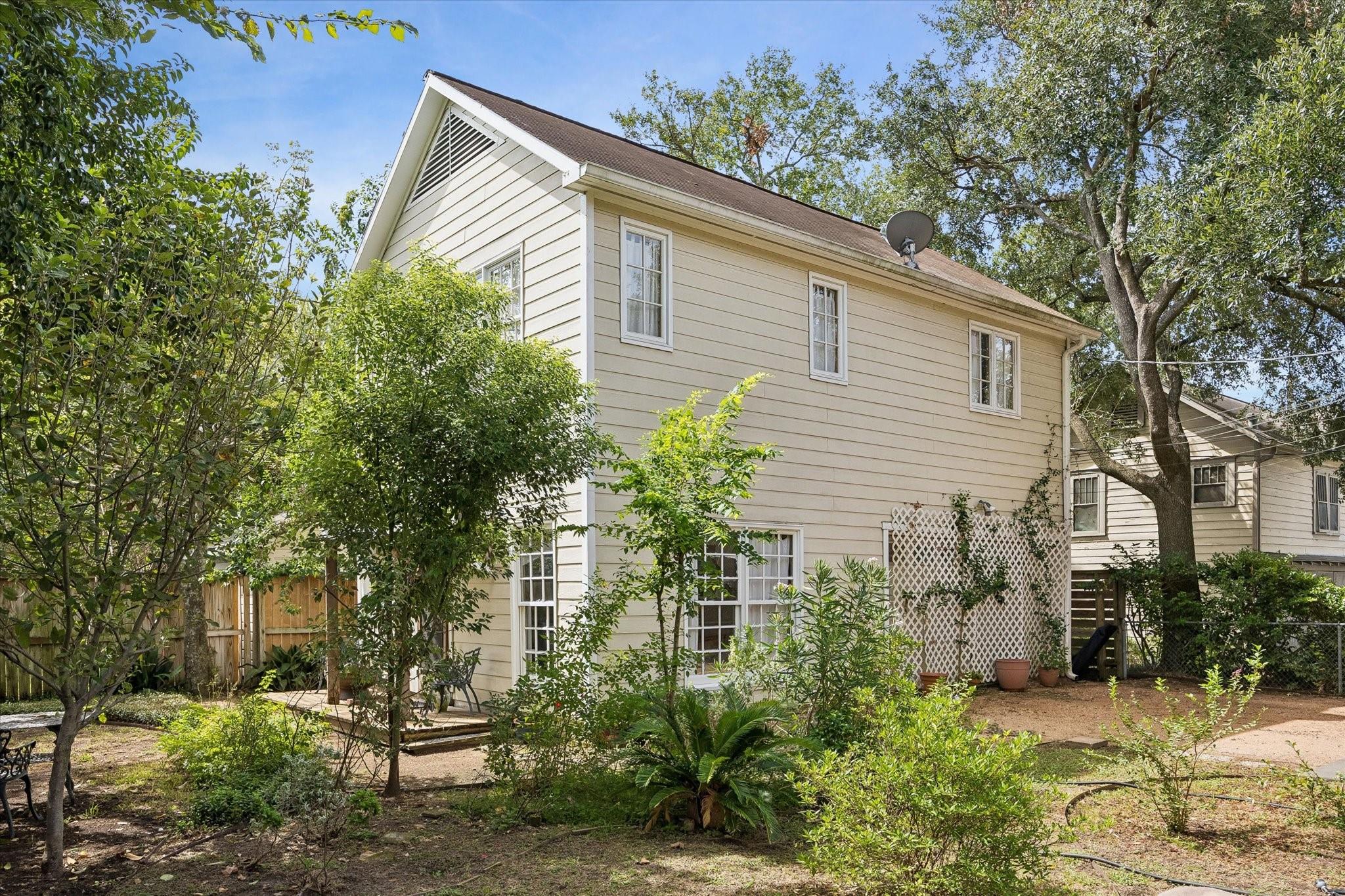 Two-story beige house seen from a leafy backyard, with a small deck and white lattice panels.