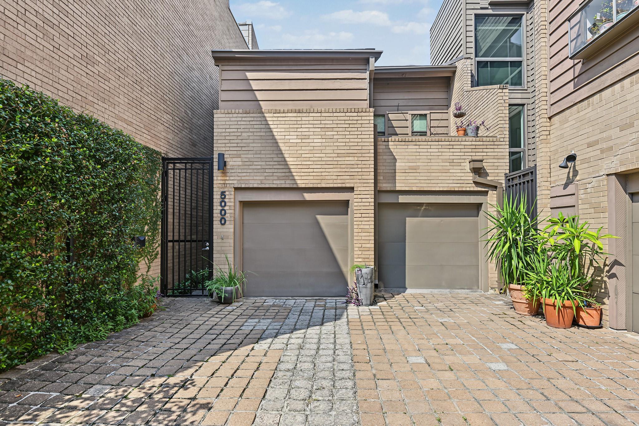 Brick townhouse exterior with two garage doors, a gated entrance, and paved driveway.