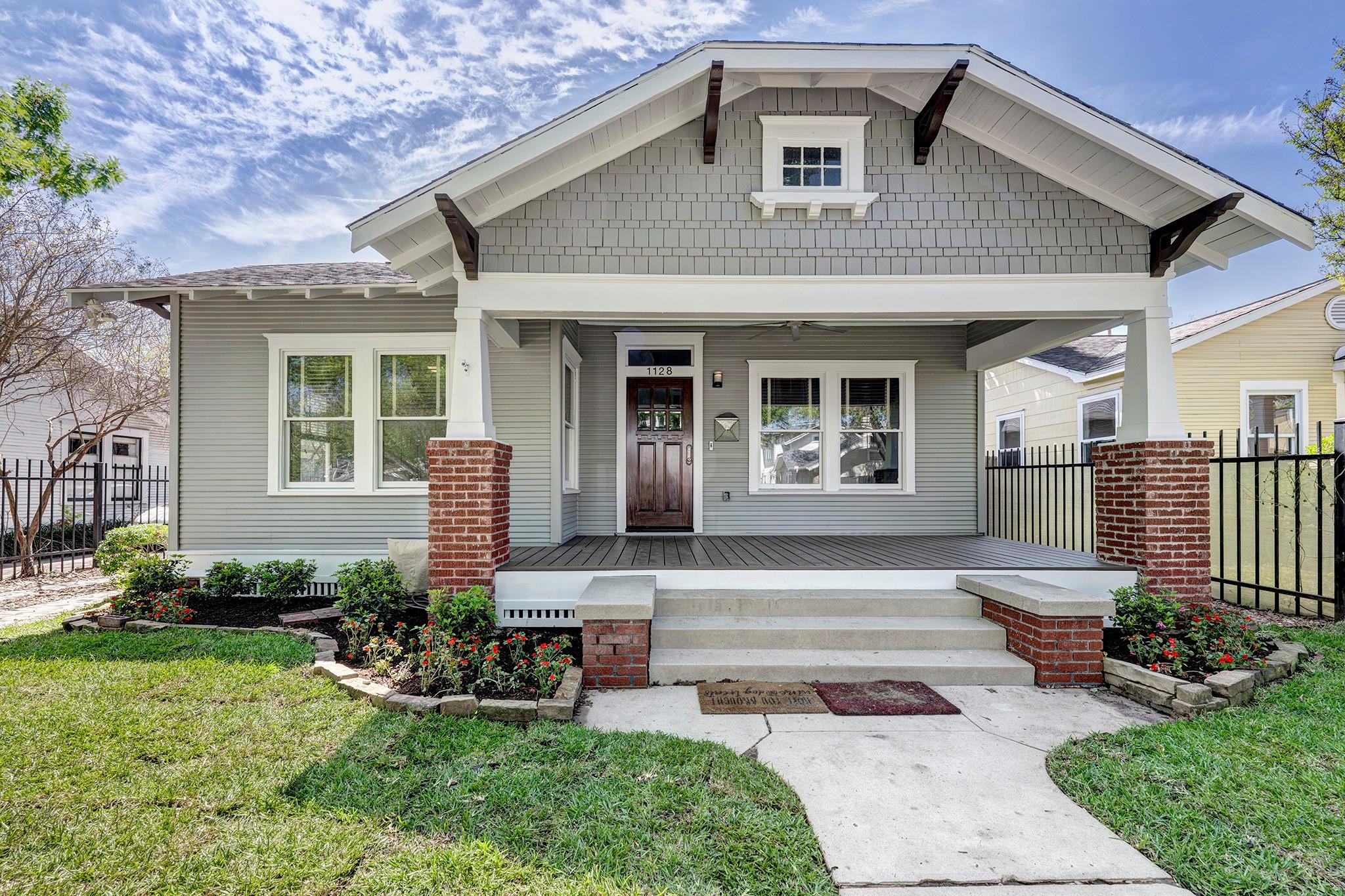 Gray house with a broad covered porch, brick column bases, and landscaped flower beds.